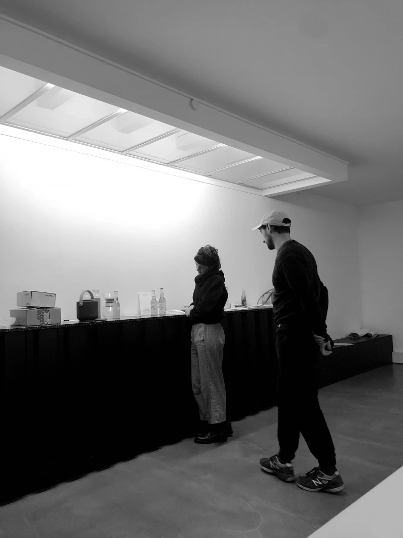 A monochrome photo of the studio space of WAF GMBH. Two people are standing in front of a long counter made from black folded steel.