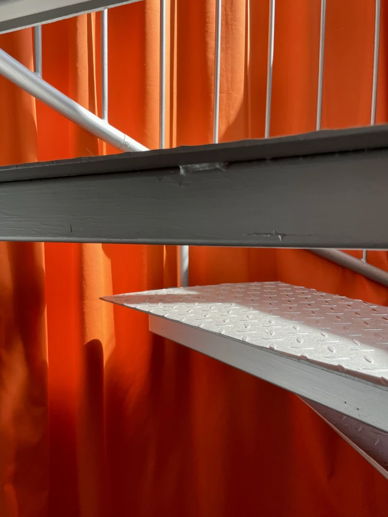 A close-up photo of a metal staircase against a cloth backdrop in international orange, photographed at the studio of WAF GMBH.